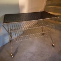 Table basse des années 1950 : chariot de service en métal doré, doté d'un plateau en maille noire et d'une étagère en fil métallique, monté sur roulettes. Brocante 93
